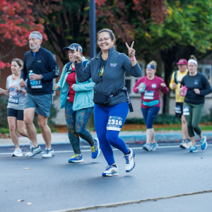 A runner smiles at the camera, her hands giving peace signs, and other runners in the 2023 Reading Hospital Road Run West Reading, PA