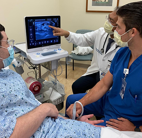 Physical medicine and rehabilitation physicians performing musculoskeletal ultrasound on patient with one physician pointing at screen