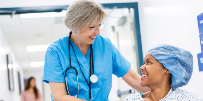 Elderly physician assists smiling female patient in hospital gown 