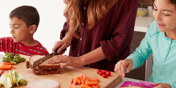 Woman cutting vegetables and preparing sandwiches with two kids