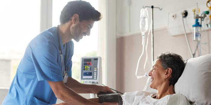 Clinician taking patient's blood pressure in hospital bed. 