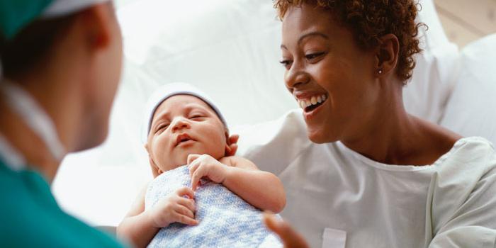 Woman holding newborn baby being handed over by doctor