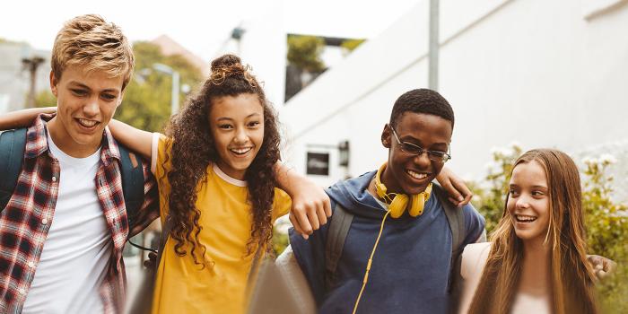 Four adolescent friends laughing while walking together outdoors