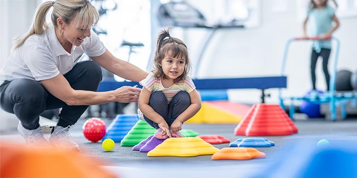 Little girl doing balance exercise in rehabilitation facility with rehab staff member in background