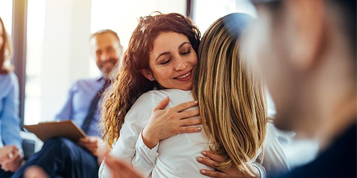 Middle-aged woman in support group setting getting hug from another woman