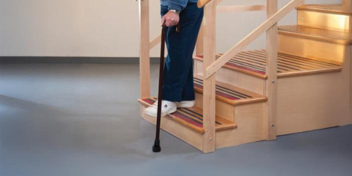 A person's hand grips onto the railing as they step down stairs one leg at a time - using the non-operated leg first, followed by the operated leg.