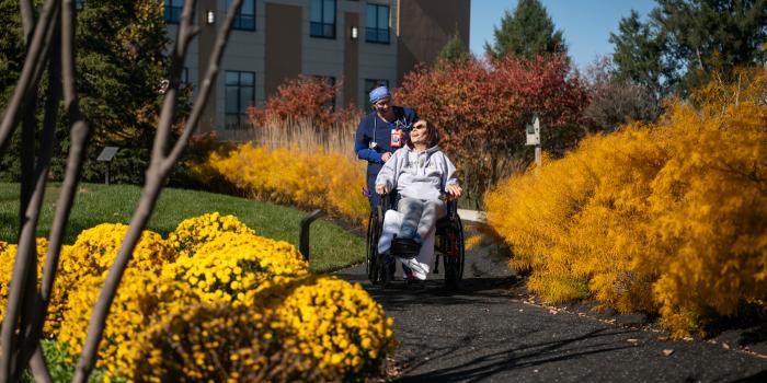 A nurse pushes a patient in a wheelchair through an autumn garden