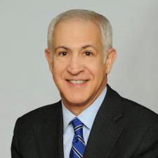 Headshot of caucasian male with gray hair wearing a dark suit.