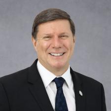 Headshot of Charles Cairns, caucasian male with brown hair wearing a dark suit.